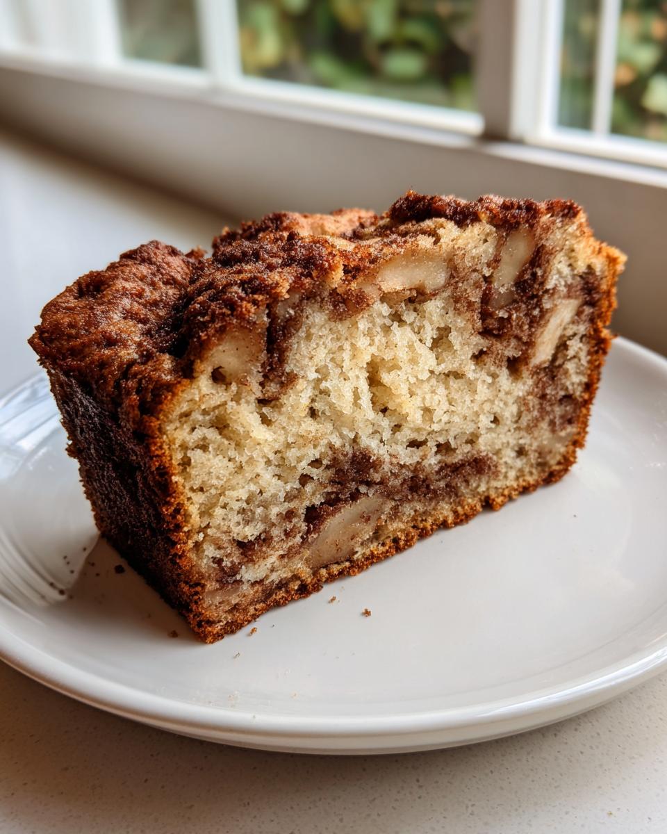 A thick slice of moist apple bread featuring visible apple chunks and a rich cinnamon swirl topping.