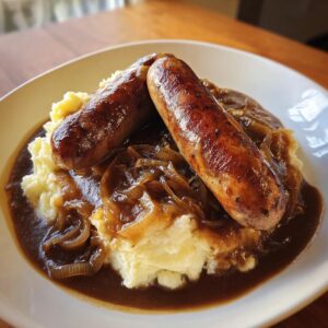 Two perfectly browned sausages resting on creamy mashed potatoes covered in rich onion gravy for classic bangers and mash.