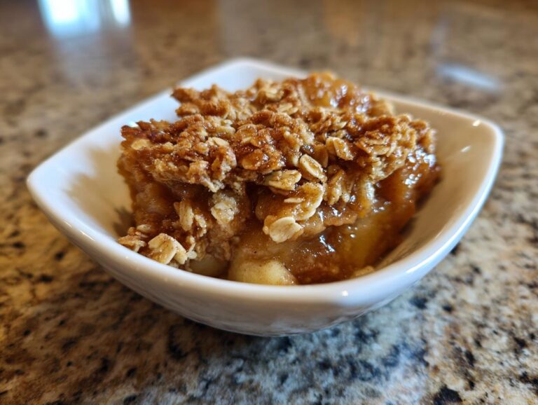 Close-up of a single serving of apple crisp recipe in a white bowl, showing gooey apples and crunchy oat topping.