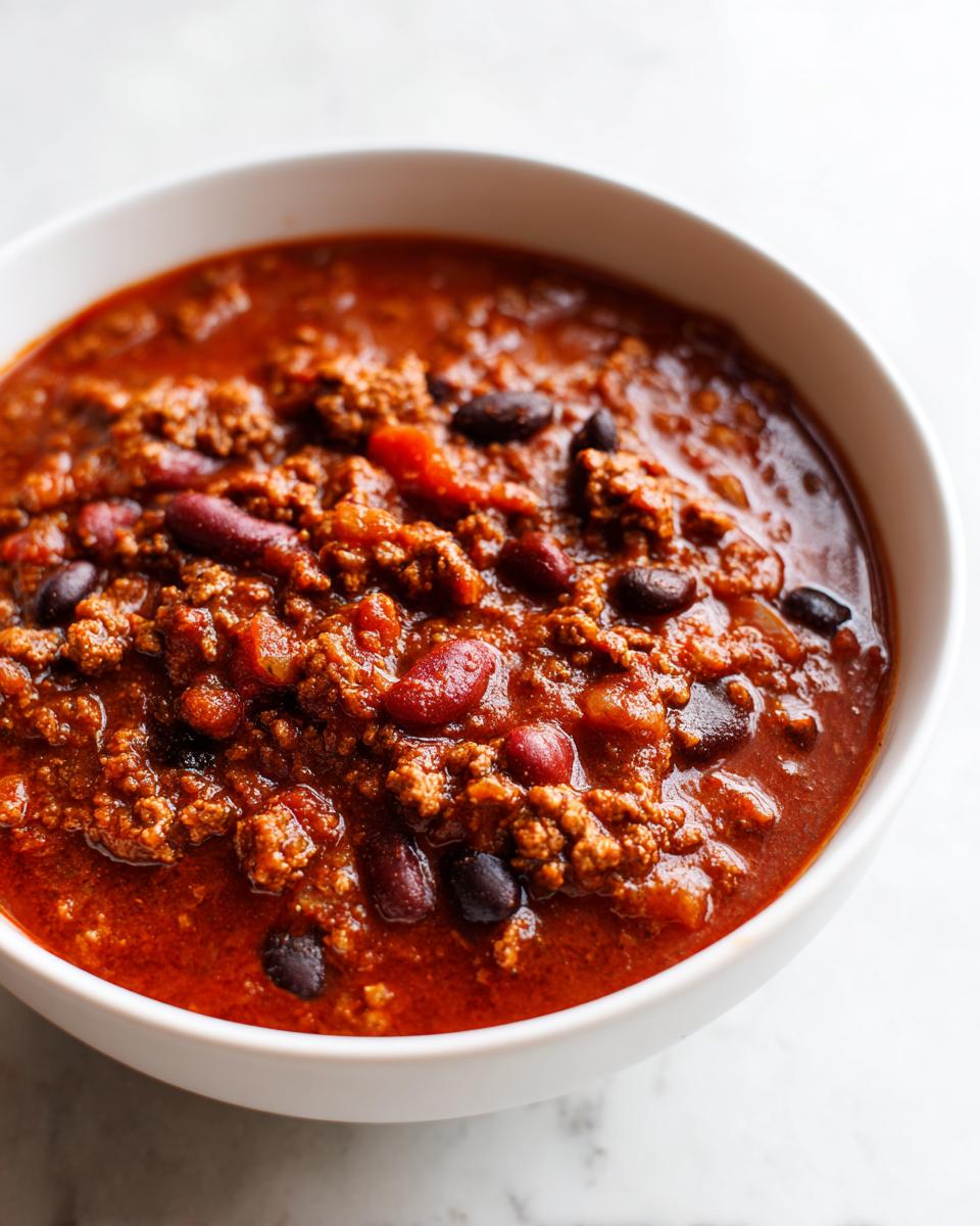Close-up of a white bowl filled with rich, thick high protein chili featuring ground meat and kidney and black beans.