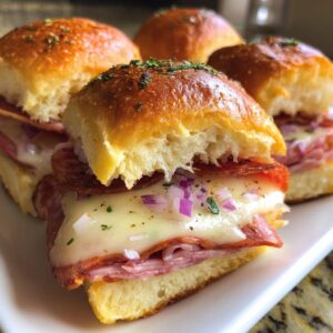 Close-up of delicious grinder sliders stacked with melted cheese, salami, ham, and topped with diced red onion.