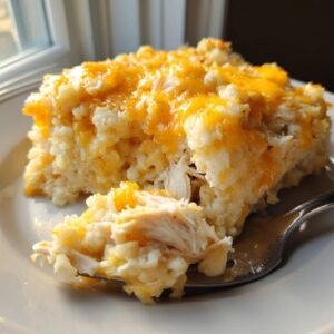Close-up of a serving of chicken cauliflower rice casserole topped with melted cheddar cheese, with a fork lifting a piece.