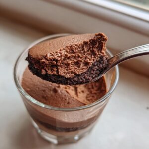A spoonful of airy, rich chocolate mousse lifted from a layered glass dessert, showing its fluffy texture.