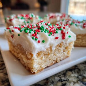 A close-up of a thick, frosted square of christmas sugar cookie bars topped with red, green, and white sprinkles.