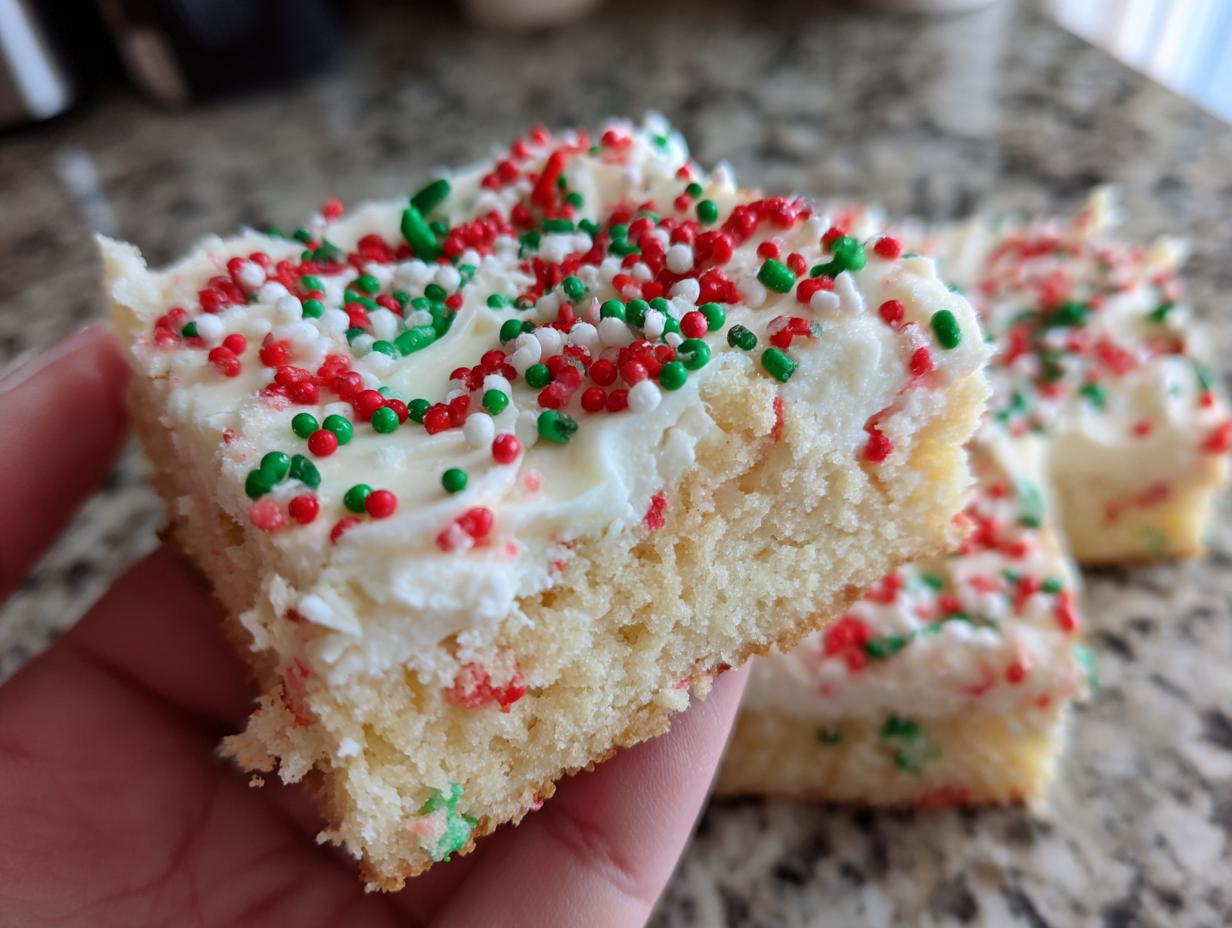 A hand holding a square slice of soft christmas sugar cookie bars topped with white frosting and red, white, and green sprinkles.