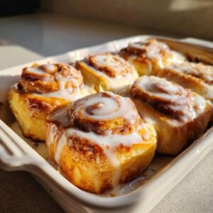 Close-up of six freshly baked cinnamon rolls with thick white icing, made using heavy cream.