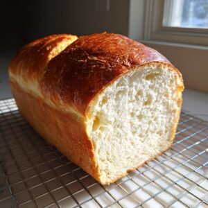 A golden-brown loaf of soft condensed milk bread, sliced to show the fluffy white interior, resting on a cooling rack.