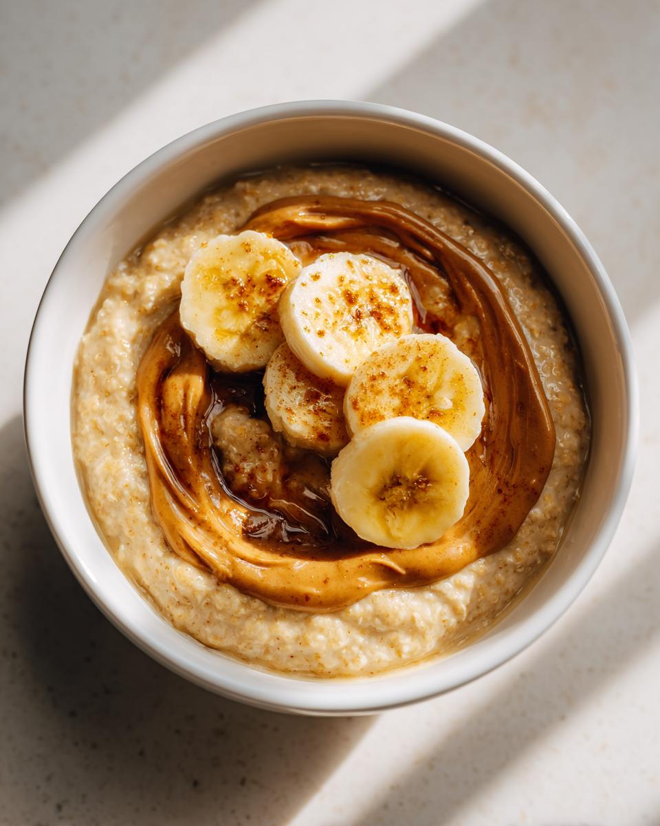 Overhead view of creamy banana oatmeal topped with a swirl of peanut butter and sliced bananas sprinkled with cinnamon.