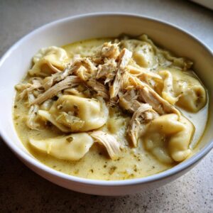 Close-up of creamy chicken and dumplings in a white bowl, topped with shredded chicken and herbs.