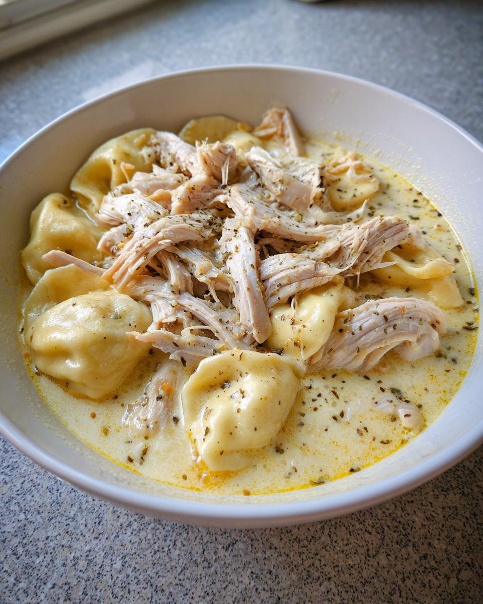 Close-up of creamy chicken and dumplings in a white bowl, topped with shredded chicken and herbs.