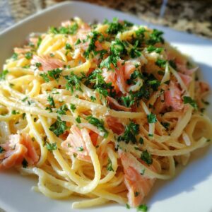 Close-up of creamy pasta tossed with pink flakes of smoked salmon and topped with fresh chopped parsley.