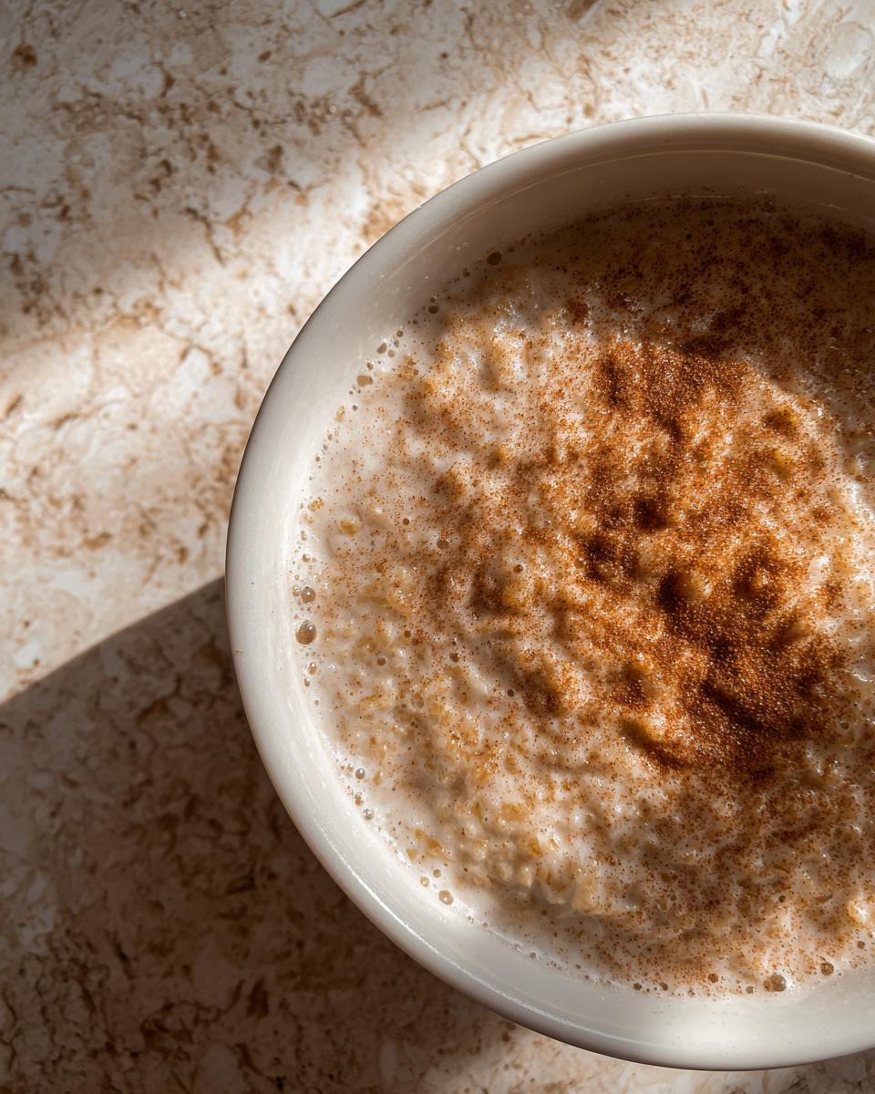 Overhead close-up of creamy rice pudding recipe in a white bowl, dusted generously with cinnamon.