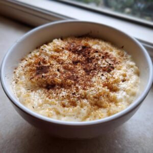 A close-up shot of creamy rice pudding recipe served in a white bowl, generously dusted with cinnamon.