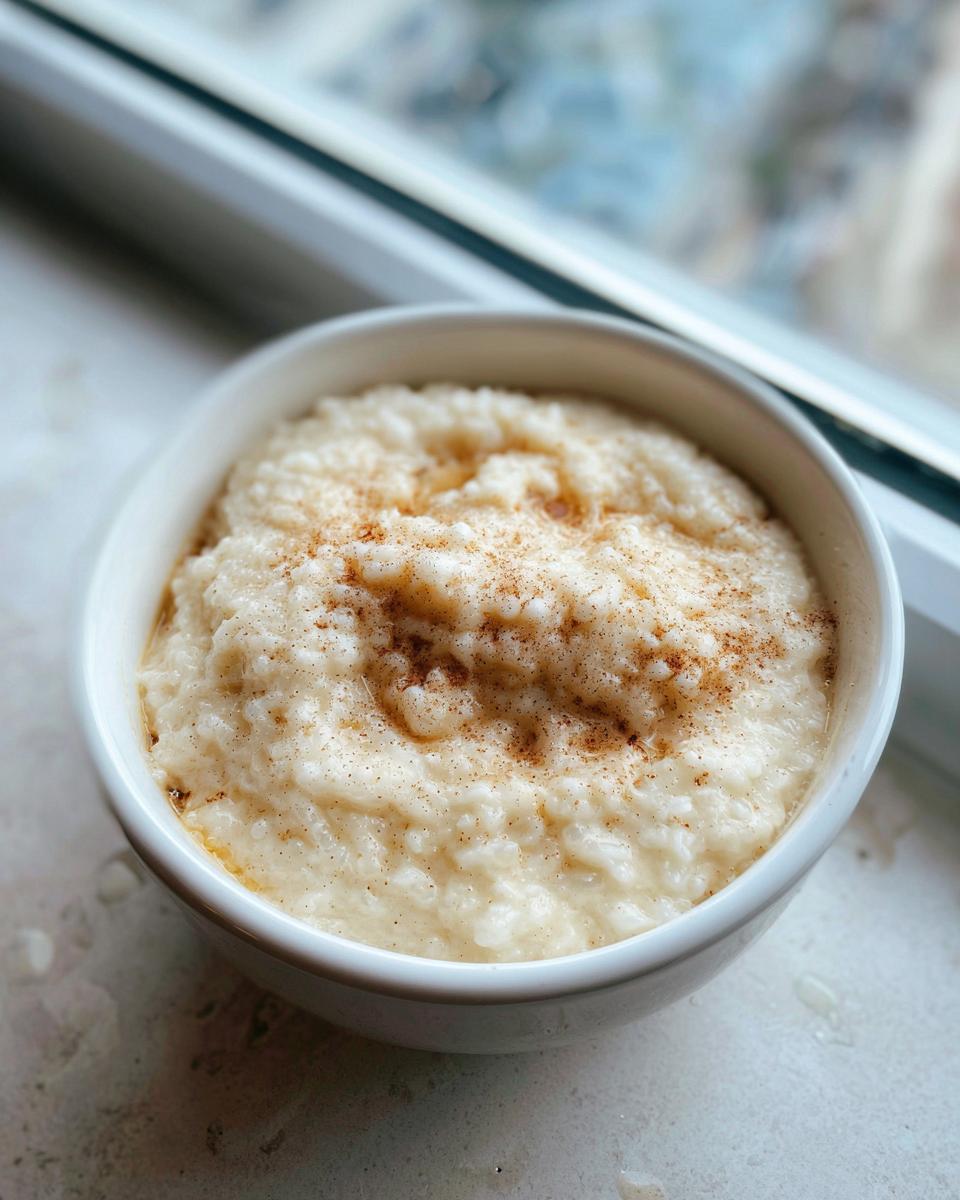 A close-up of creamy rice pudding recipe served in a white bowl, dusted with cinnamon.