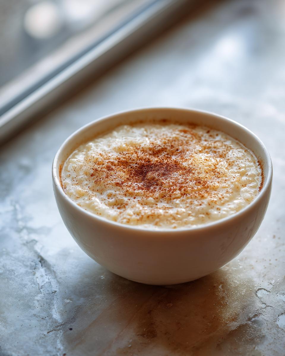 A close-up of a white bowl filled with creamy rice pudding recipe, dusted generously with cinnamon.