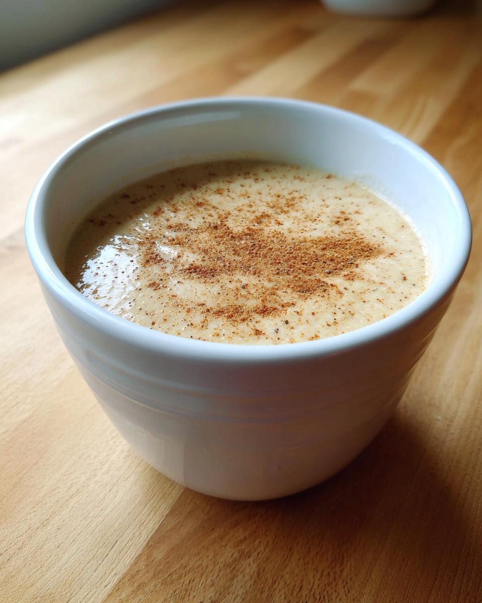 A close-up of creamy roasted cauliflower soup in a white bowl, topped with a sprinkle of brown spice.
