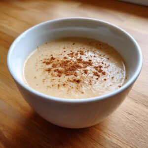 A close-up of creamy roasted cauliflower soup in a white bowl, garnished with a sprinkle of brown spice.