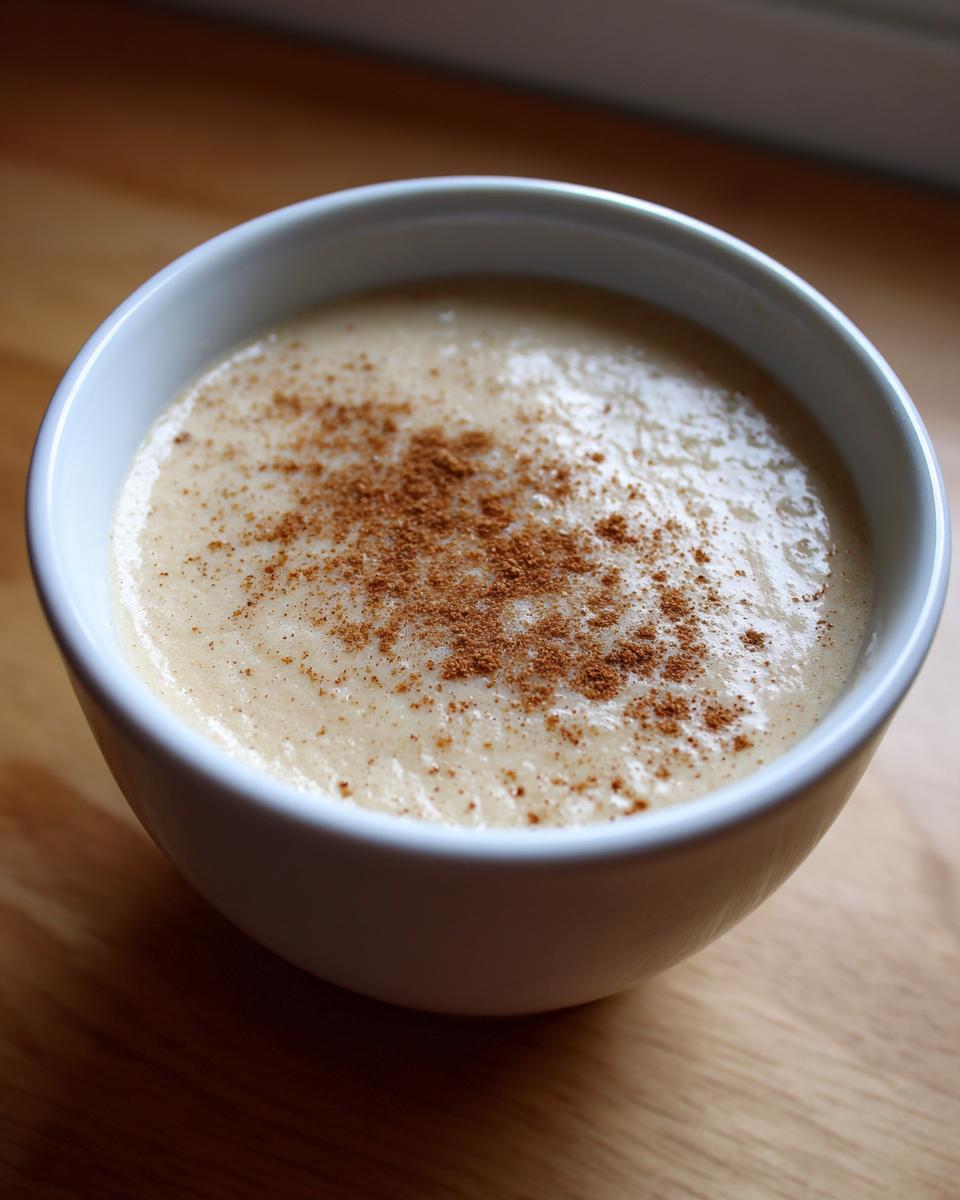 Close-up of a bowl of creamy roasted cauliflower soup, topped with a sprinkle of brown spice.