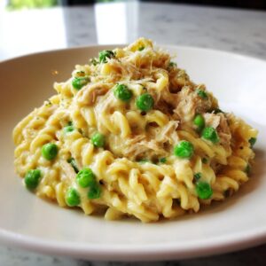 Close-up of creamy tuna pasta mixed with bright green peas, topped with shredded cheese.