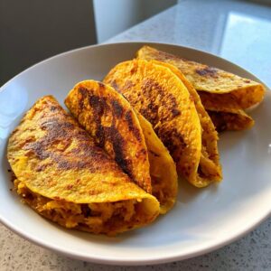 Four golden, pan-fried potato tacos filled with mashed potato mixture, served on a white plate.
