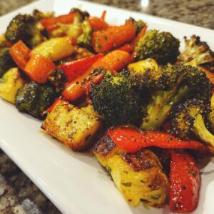 Close-up of colorful, perfectly roasted vegetables including charred broccoli, carrots, and potatoes seasoned with herbs.