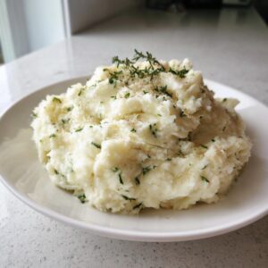 A generous serving of creamy Boursin mashed potatoes topped with fresh thyme and cracked pepper.