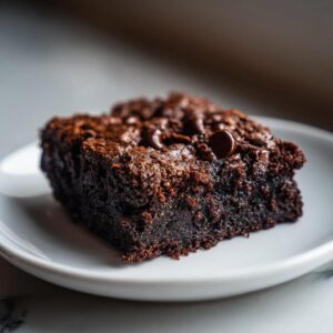 A single, rich, fudgy square of date brownies topped with chocolate chips on a white plate.