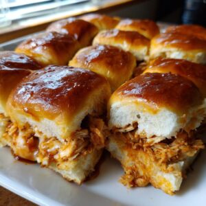 A close-up of several glistening, glazed bbq chicken sliders filled with saucy shredded chicken on a white serving platter.