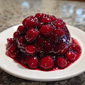 A mound of glossy, deep red homemade cherry pie filling served on a white plate.