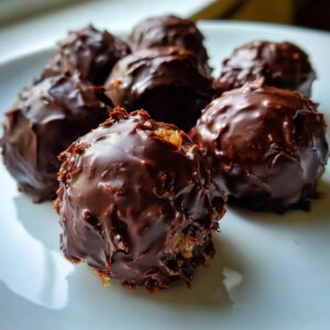 Close-up of several rich, dark chocolate-coated almond joy truffles resting on a white plate.