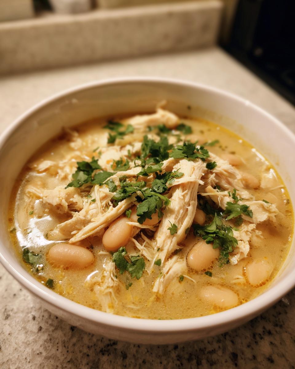 Close-up of a bowl of creamy instant pot white chicken chili topped with shredded chicken, white beans, and fresh cilantro.