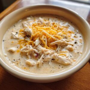 A close-up of a creamy bowl of keto white chicken chili topped generously with shredded cheddar cheese.
