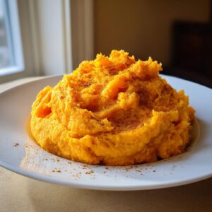 A generous serving of bright orange mashed sweet potatoes topped with ground cinnamon on a white plate.