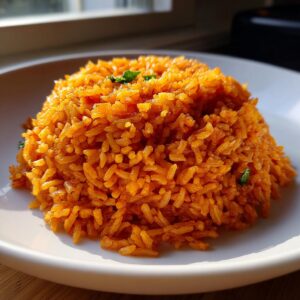 A mound of vibrant orange Mexican rice recipe served on a white plate, garnished with a few flecks of green herbs.
