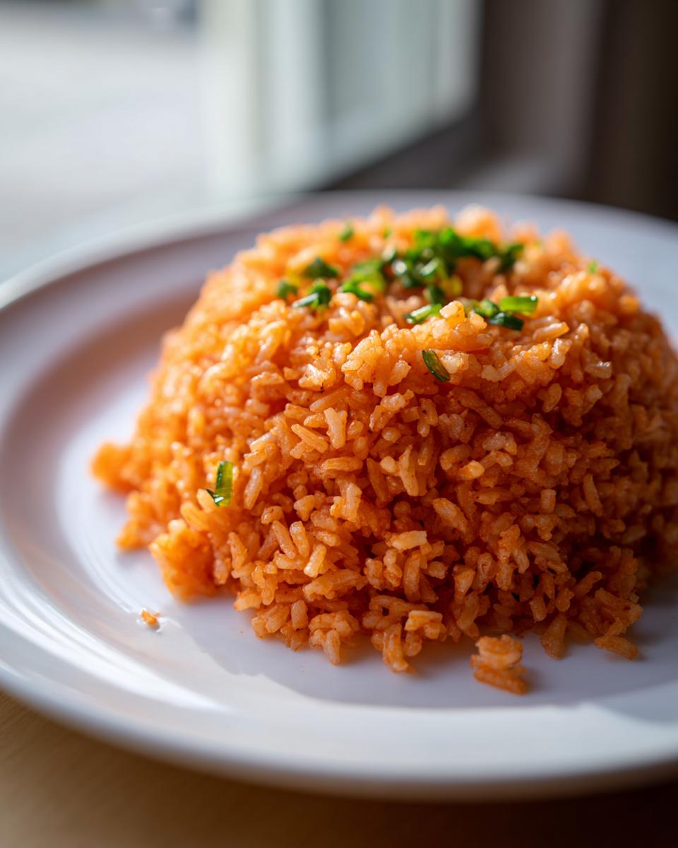 A mound of vibrant orange Mexican rice served on a white plate, topped with chopped green onions.