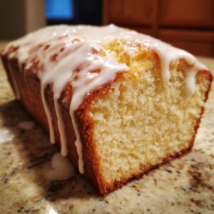 Close-up of a freshly baked lemon pound cake loaf with thick white glaze dripping down the side.