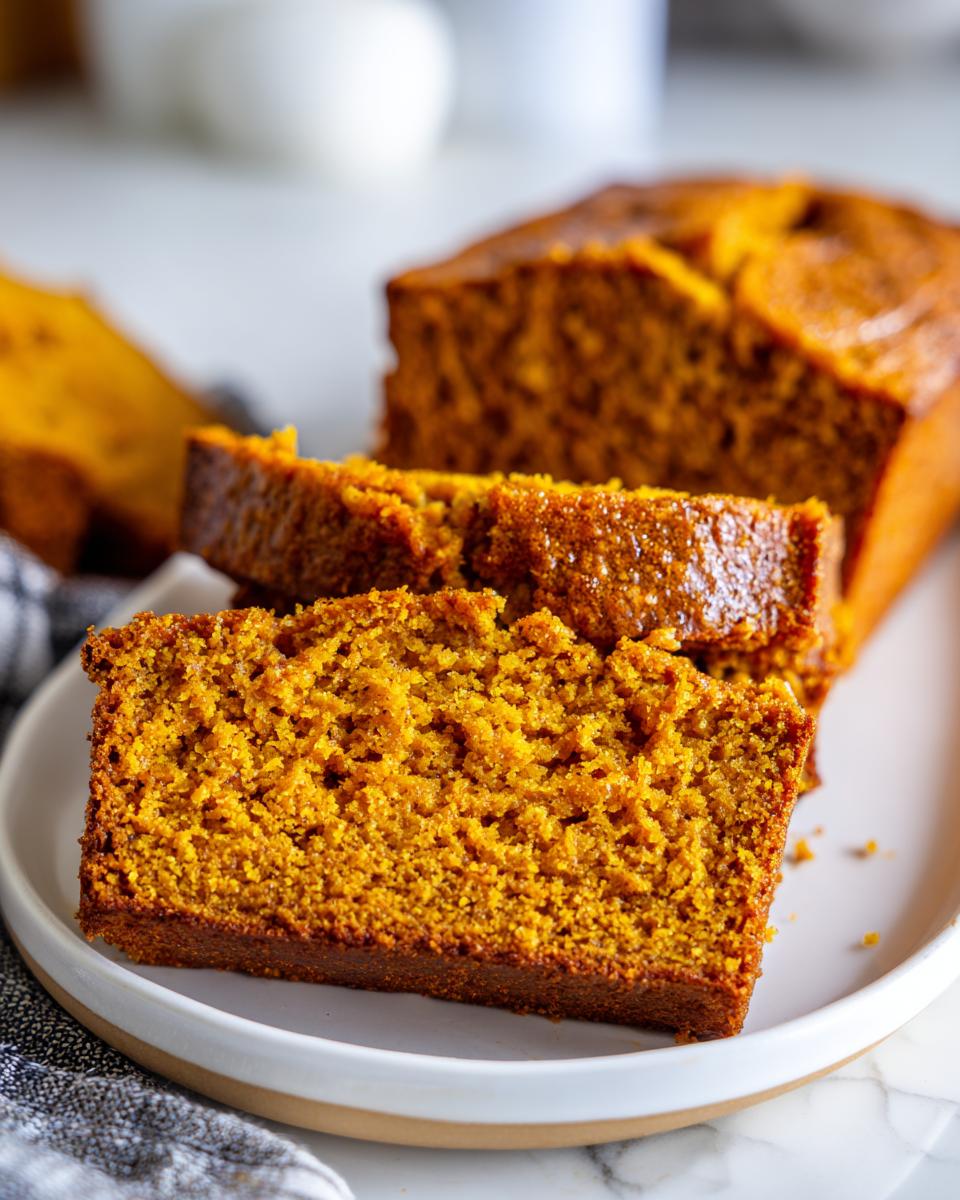 Close-up of thick, moist slices of homemade pumpkin bread displayed on a white plate.