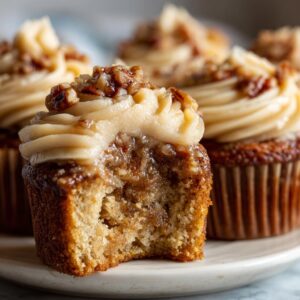 Close-up of a pecan pie cupcakes with a bite taken out, revealing the gooey filling and brown sugar frosting.