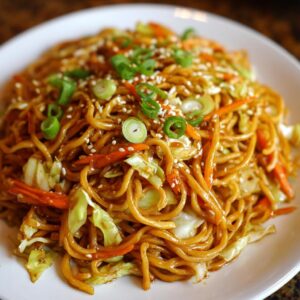 A close-up of savory fried noodles mixed with shredded cabbage and carrots, topped with green onions and sesame seeds.