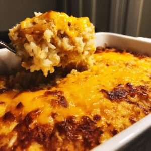 A spoonful of creamy french onion butter rice topped with melted, browned cheddar cheese being lifted from a white baking dish.