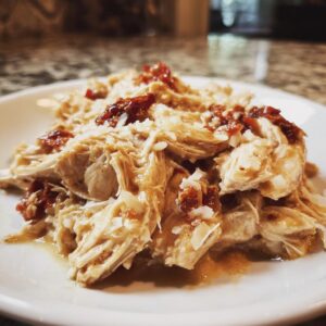 Close-up of shredded crockpot marry me chicken topped with sun-dried tomatoes and Parmesan cheese on a white plate.