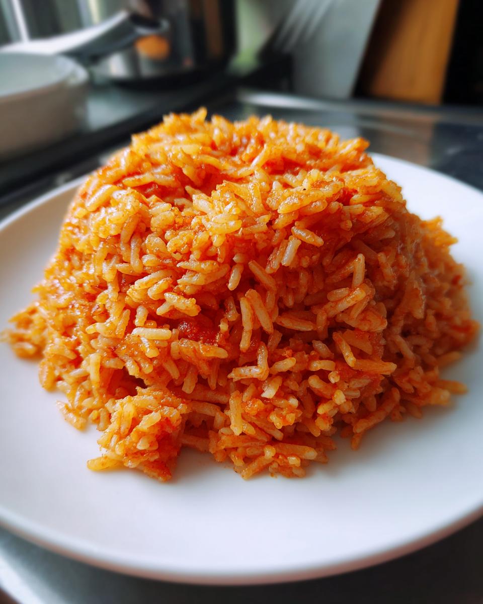 A close-up, slightly angled shot of a mound of vibrant orange-red jollof rice served on a white plate.