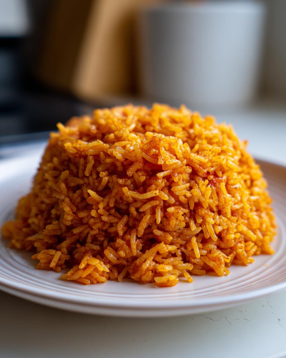 A perfectly molded mound of vibrant orange smoky jollof rice served on a white plate.