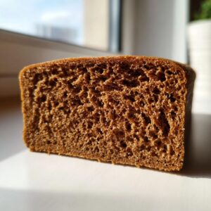 Close-up showing the dense, dark brown, and sturdy crumb texture of a piece of gingerbread used for a gingerbread house recipe.