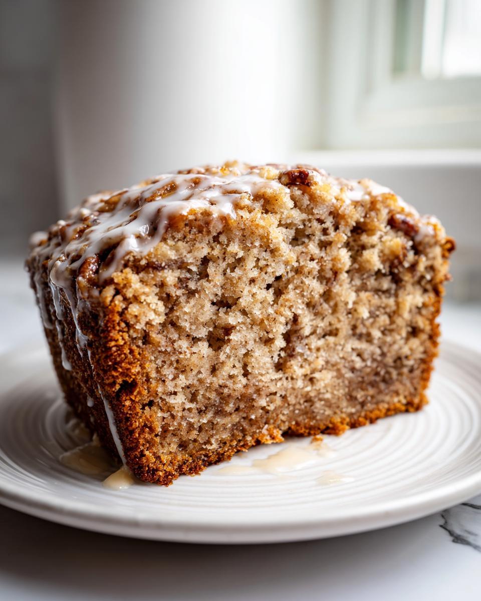 Close-up of a moist slice of sweet Alabama pecan bread topped with a dripping vanilla glaze.
