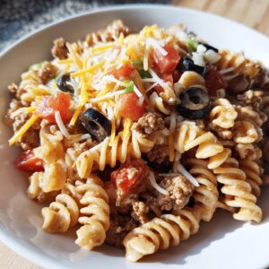 Close-up of a bowl of creamy taco pasta salad featuring rotini pasta, ground beef, tomatoes, olives, and shredded cheese.