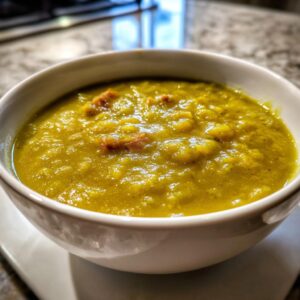 Close-up of a creamy, thick bowl of yellow-green pea soup topped with visible chunks of ham.