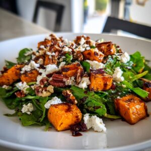 Close-up of a vibrant sweet potato salad featuring roasted sweet potato cubes, feta cheese, pecans, and greens.